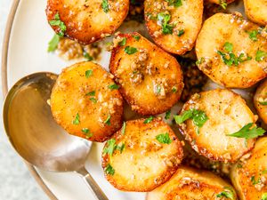 Garlic-coated roasted potatoes topped with fresh herbs on a plate with a spoon