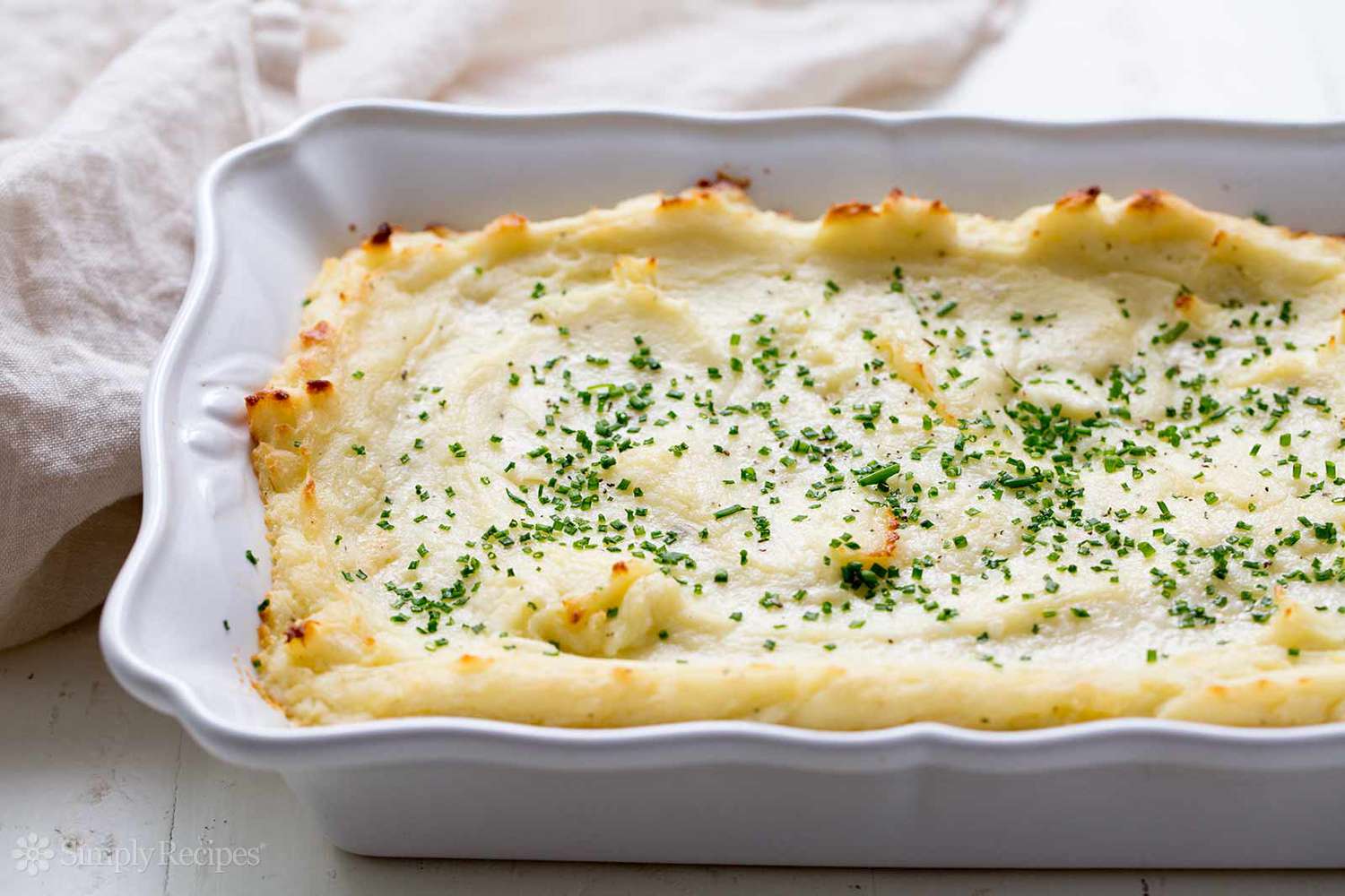 A baking dish with mashed potatoes topped with chopped herbs
