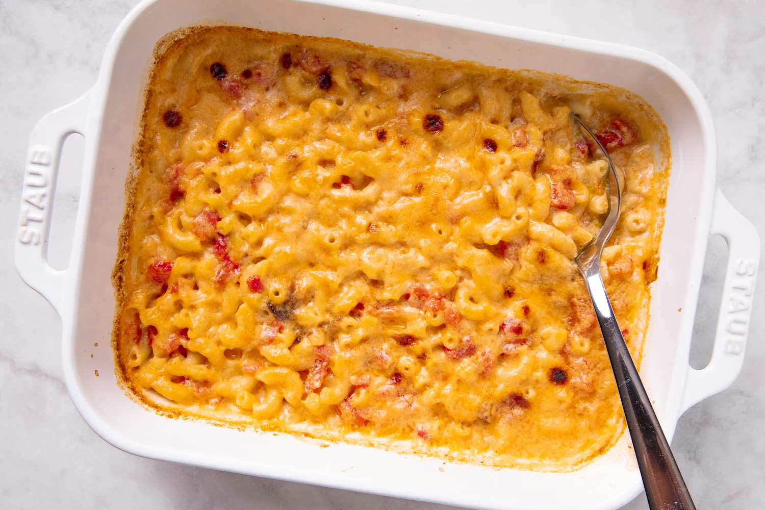 A baking dish containing macaroni and cheese with a serving spoon placed in it