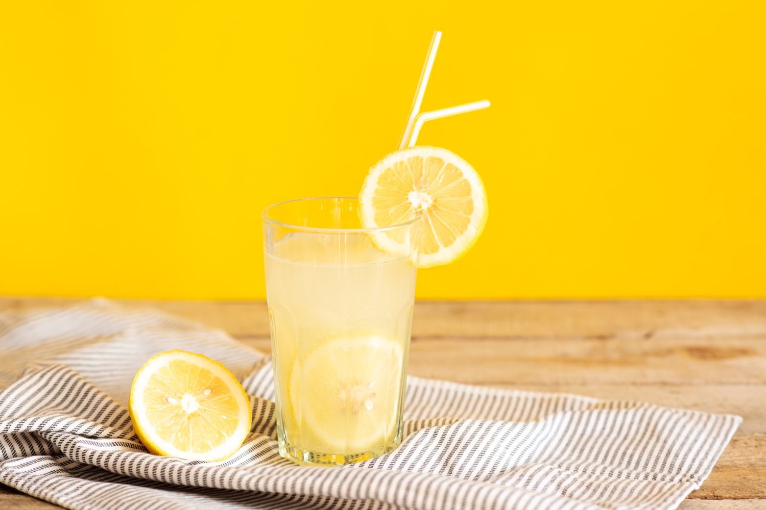 A glass of lemonade with lemon slices and straws on a striped cloth
