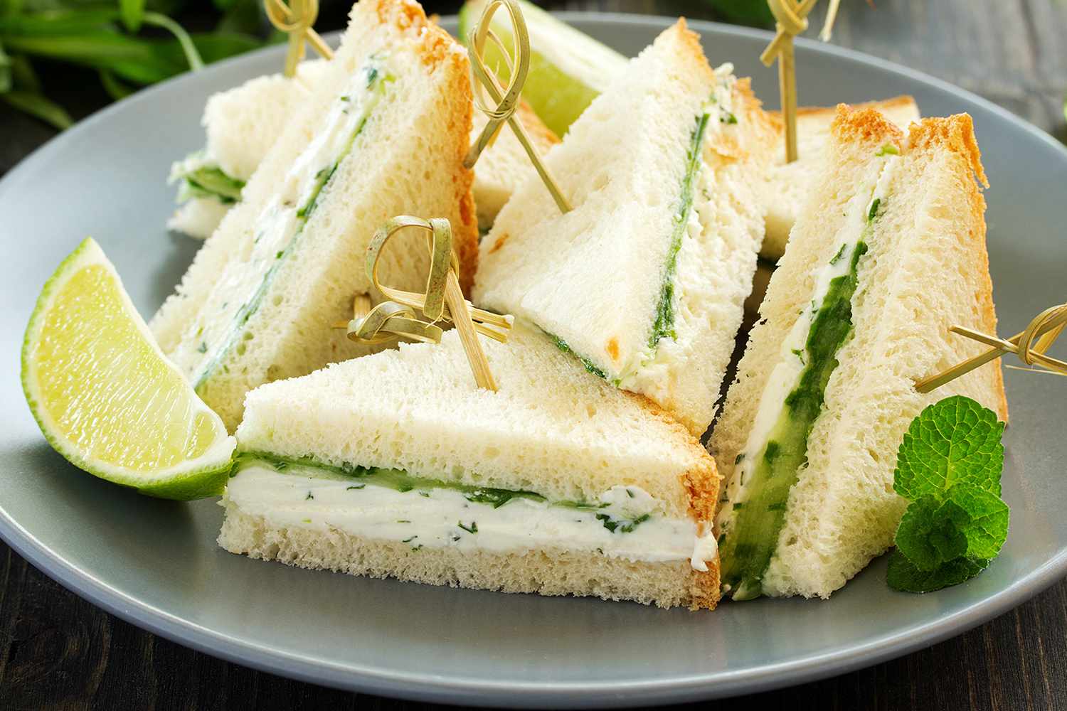 Plate with triangle-shaped cucumber sandwiches, garnished with lime and mint