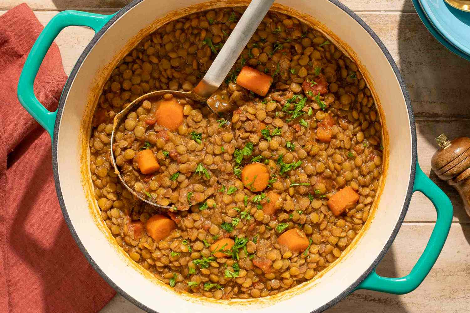 A pot of spiced lentils with carrots garnished with greens and a serving spoon inside