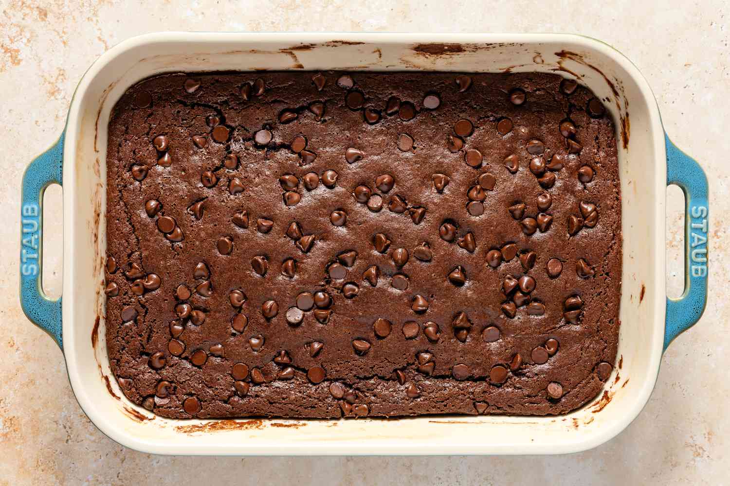 Overhead view of a baking dish of baked batter for Chocolate Dump Cake recipe on a tan countertop