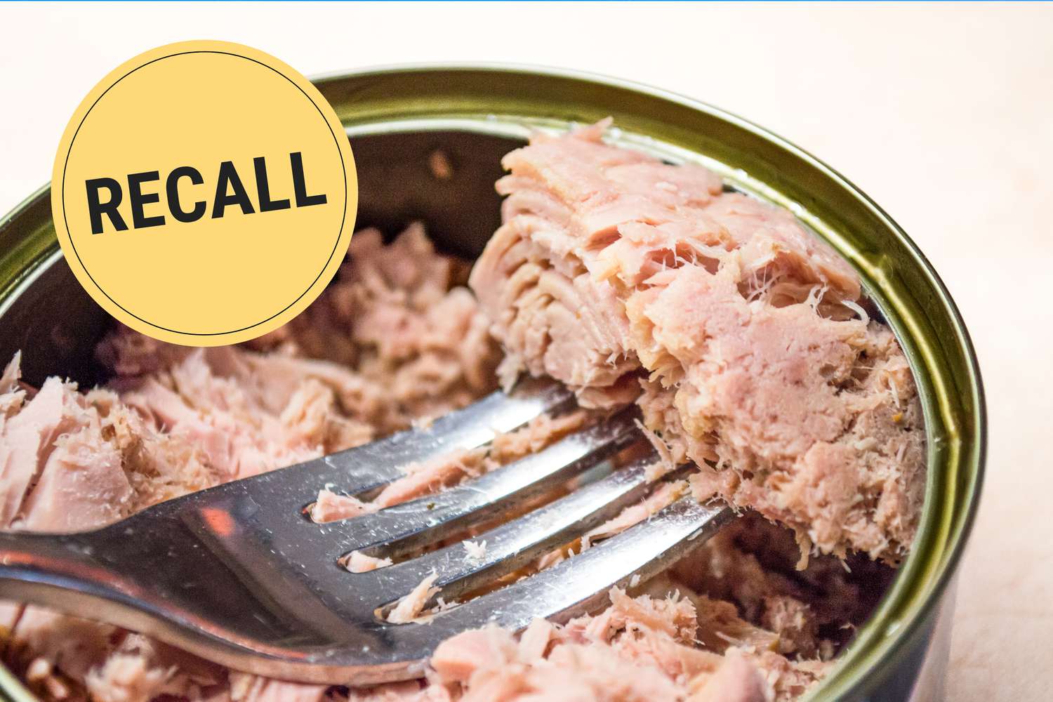 Tuna fish in a can with a fork with the word recall stamped over top