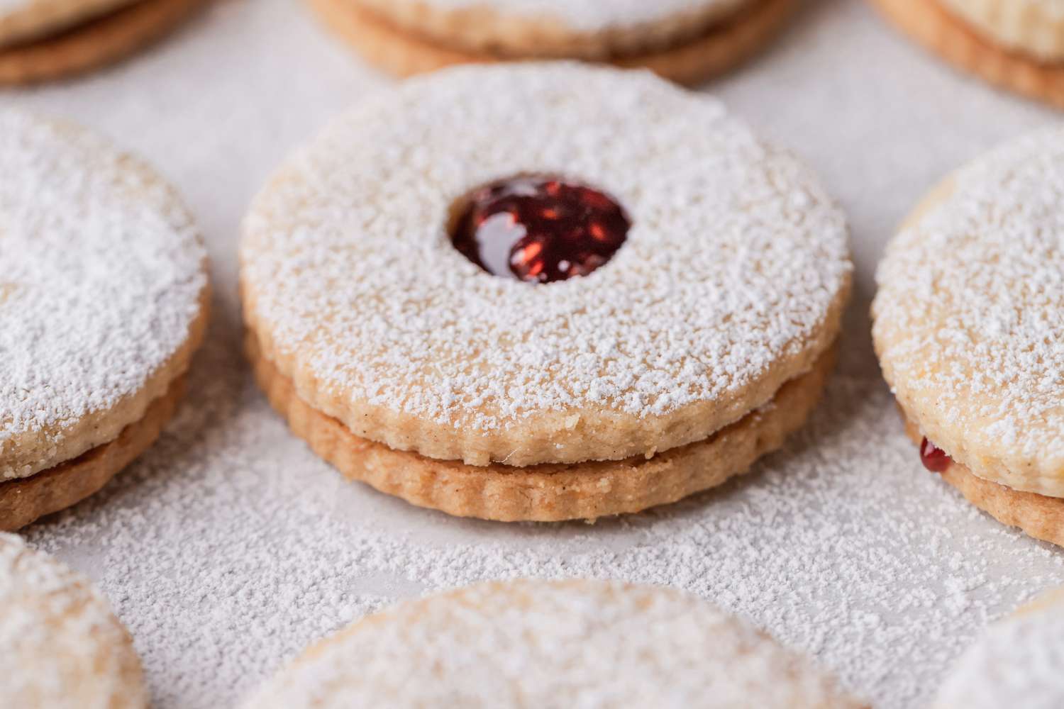 Close up of a jam filled sandwich cookie topped iwth powdered sugar.