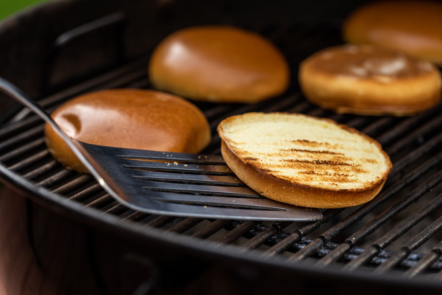Spatula with a toasted hamburger bun on a grill.