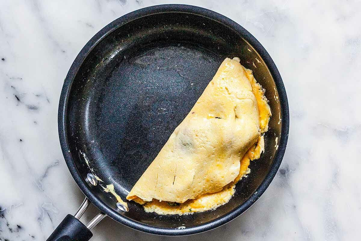 Overhead of a filled omelette being folded in half on a non-stick pan