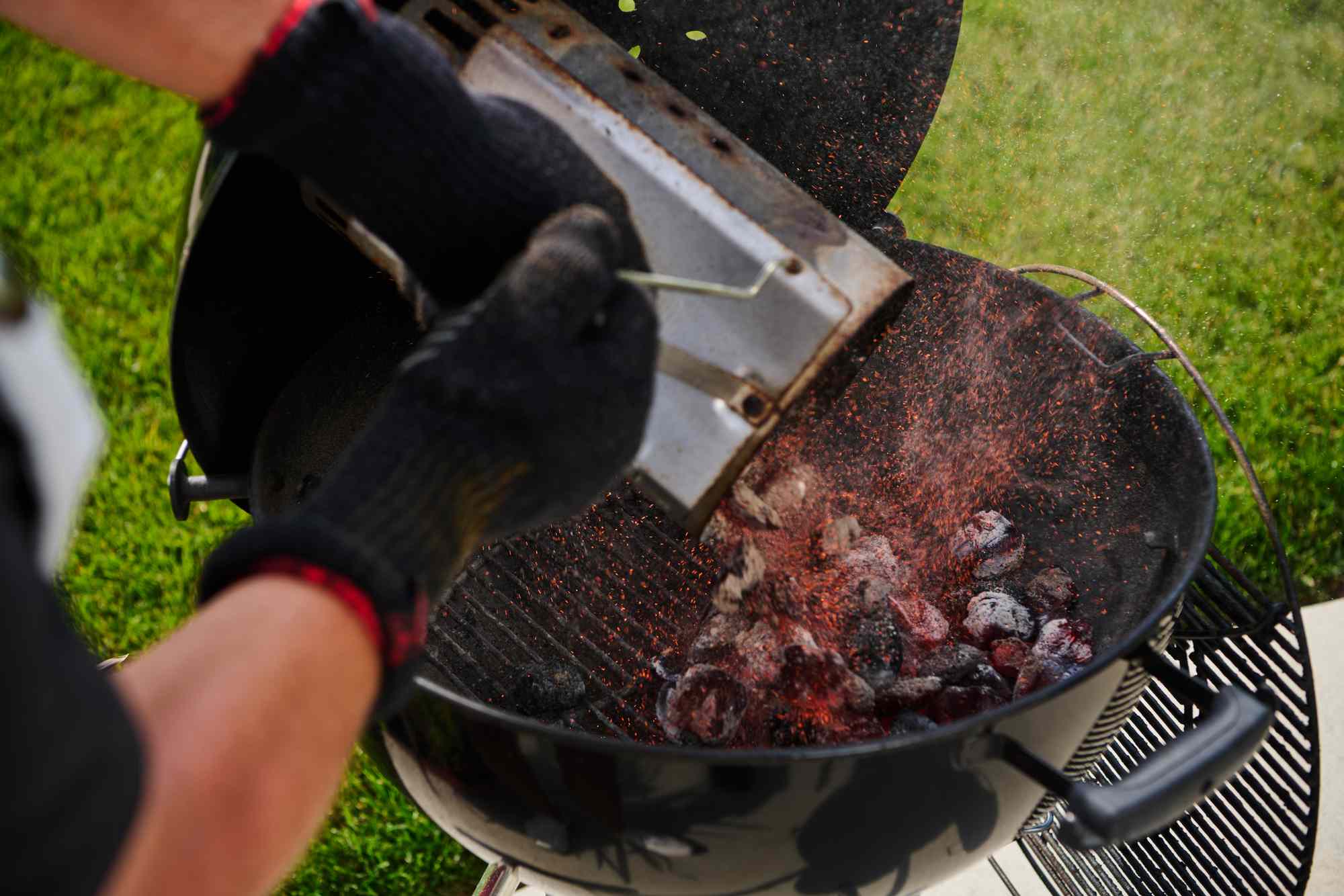 Person pouring hot coals into a grill with gloved hands