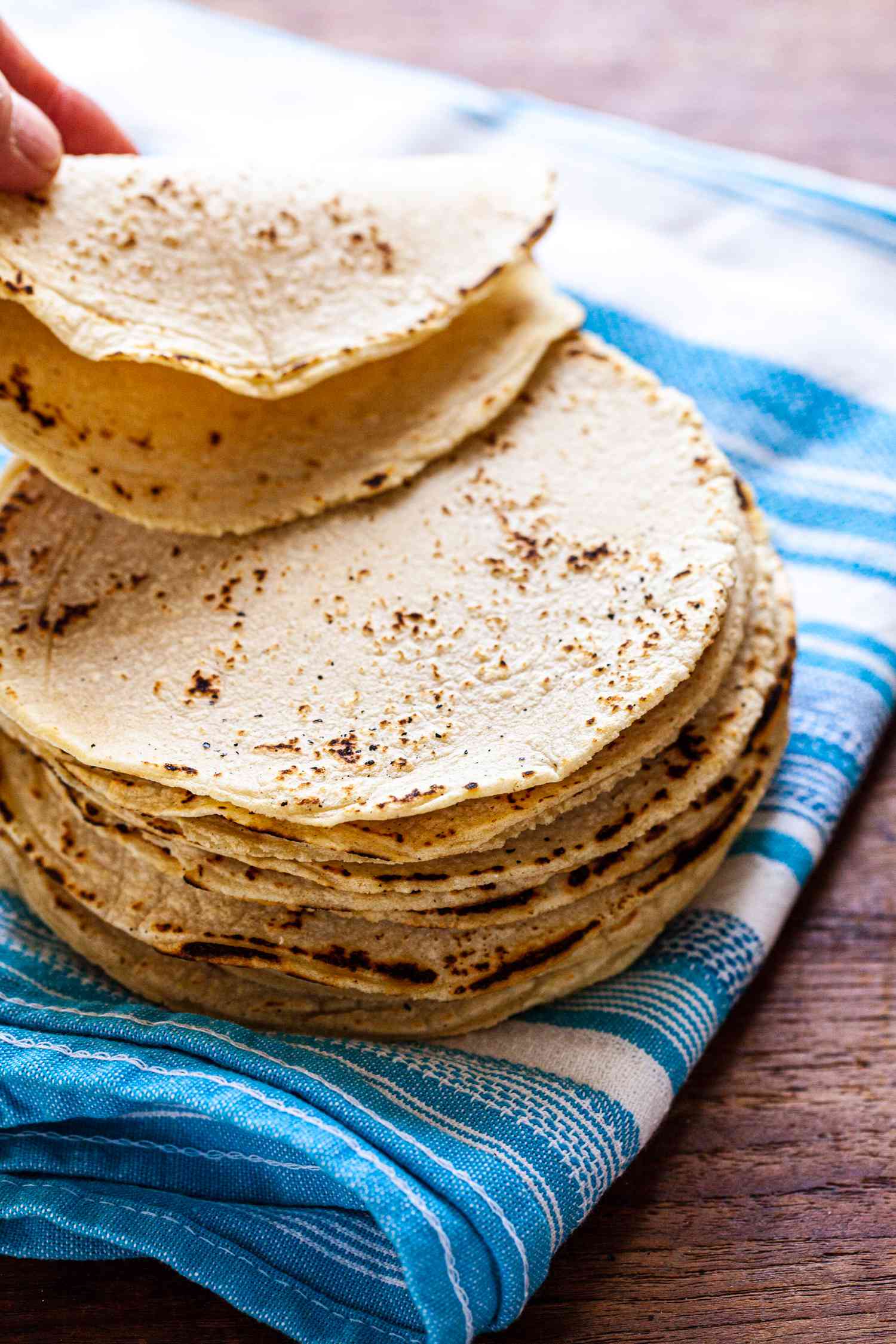 Corn tortilla recipe with corn tortillas stacked on a blue striped linen.