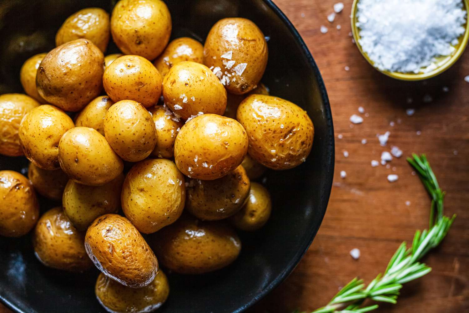 Potato confit on a black plate with salt.