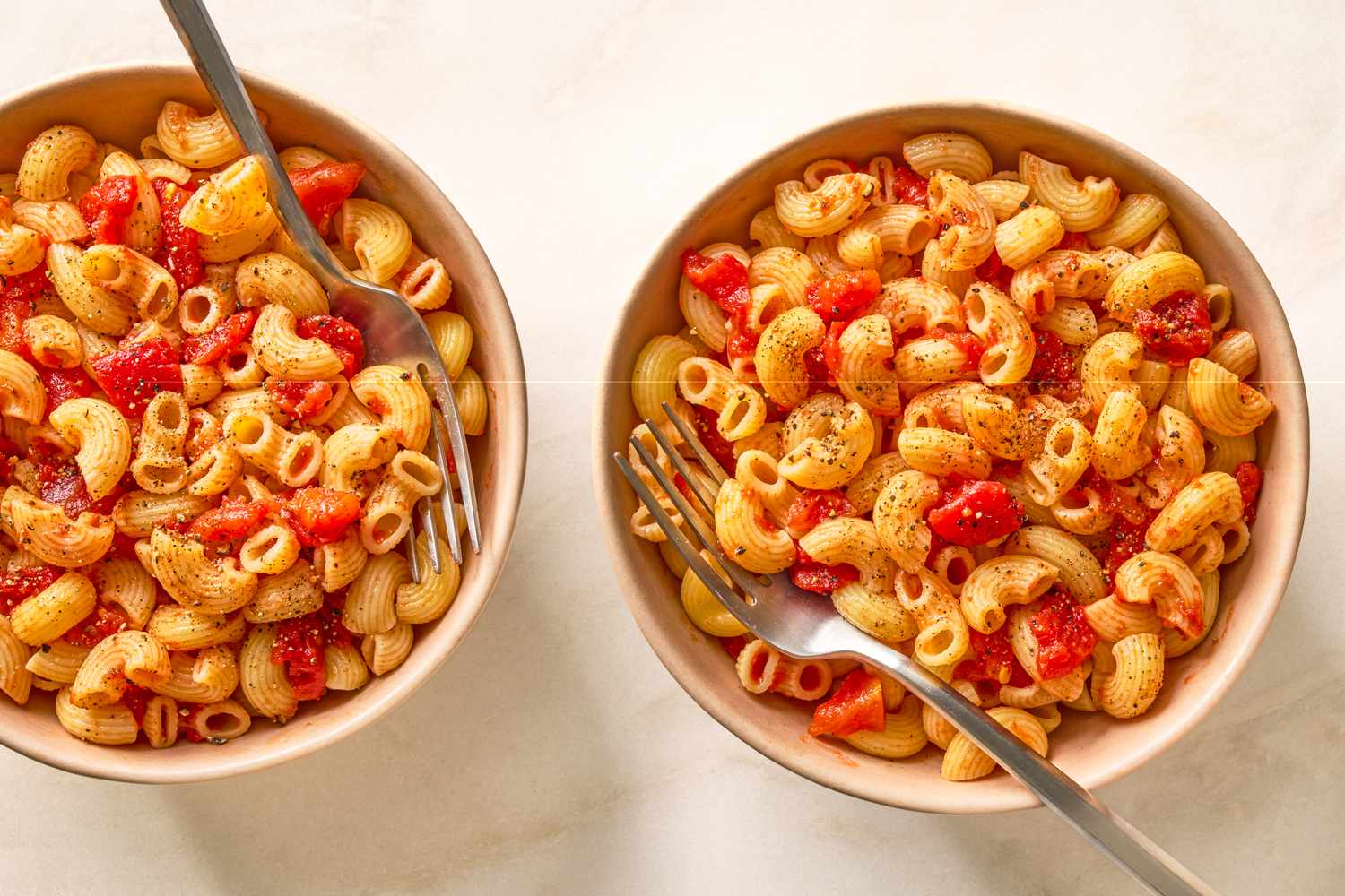 Two bowls of macaroni with tomatoes placed on a light background with forks in each bowl
