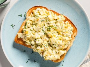 Overhead view of a dill egg salad on a piece of toast on small blue plate