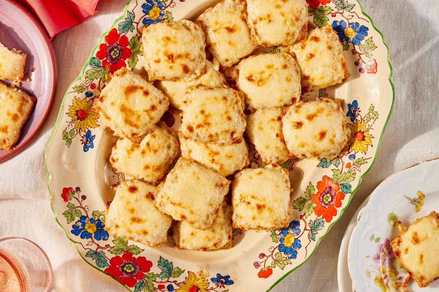 Triscuit appetizers topped with melted cheese on a serving plate with flower design