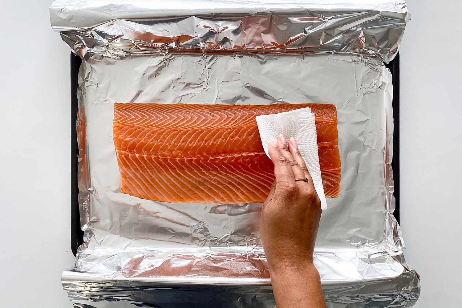 A raw salmon on a foil lined baking sheet