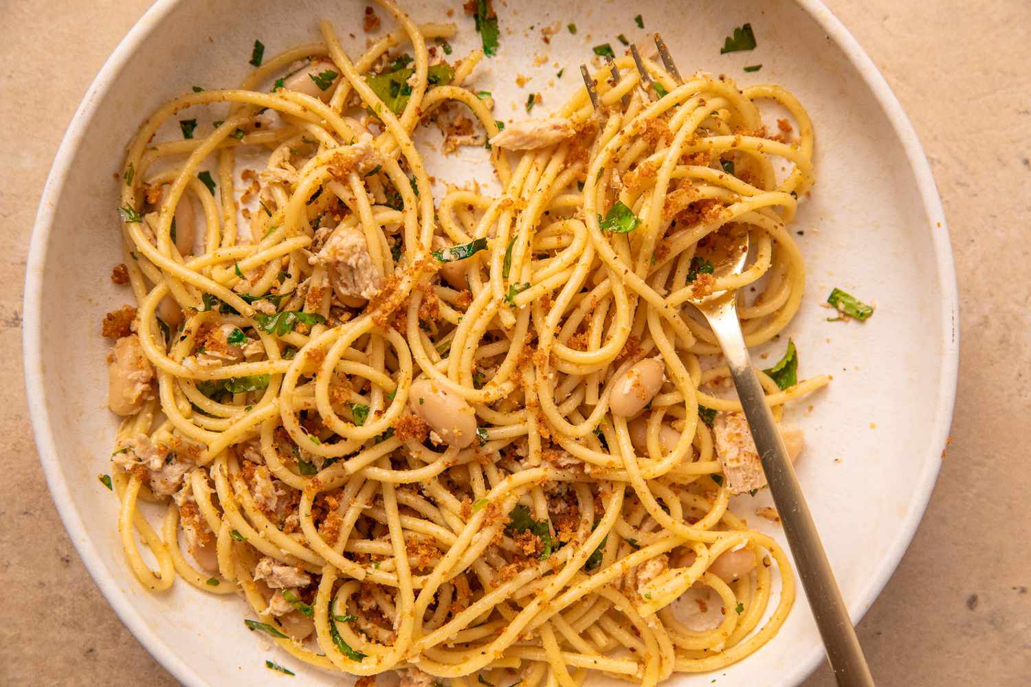 Pasta with tuna, white beans, breadcrumbs, and herbs on a plate with a fork.