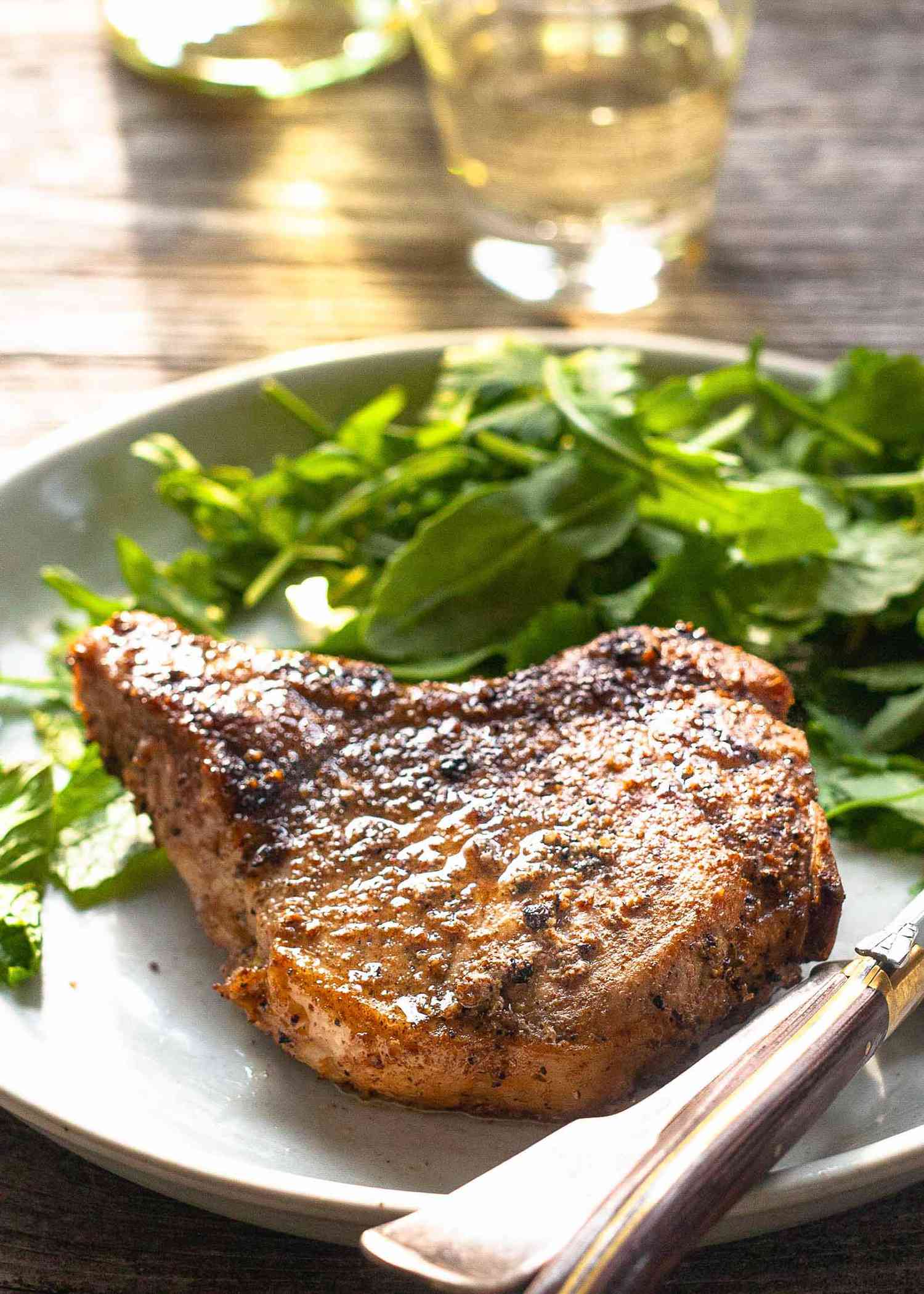 Pork chop on a plate with salad and white wine in the background