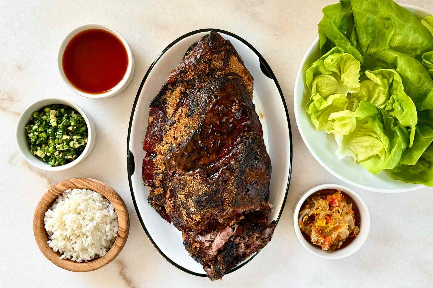 A table spread with roasted meat on a platter lettuce leaves rice and small bowls of condiments