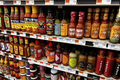 A grocery store shelf displaying a variety of hot sauce bottles
