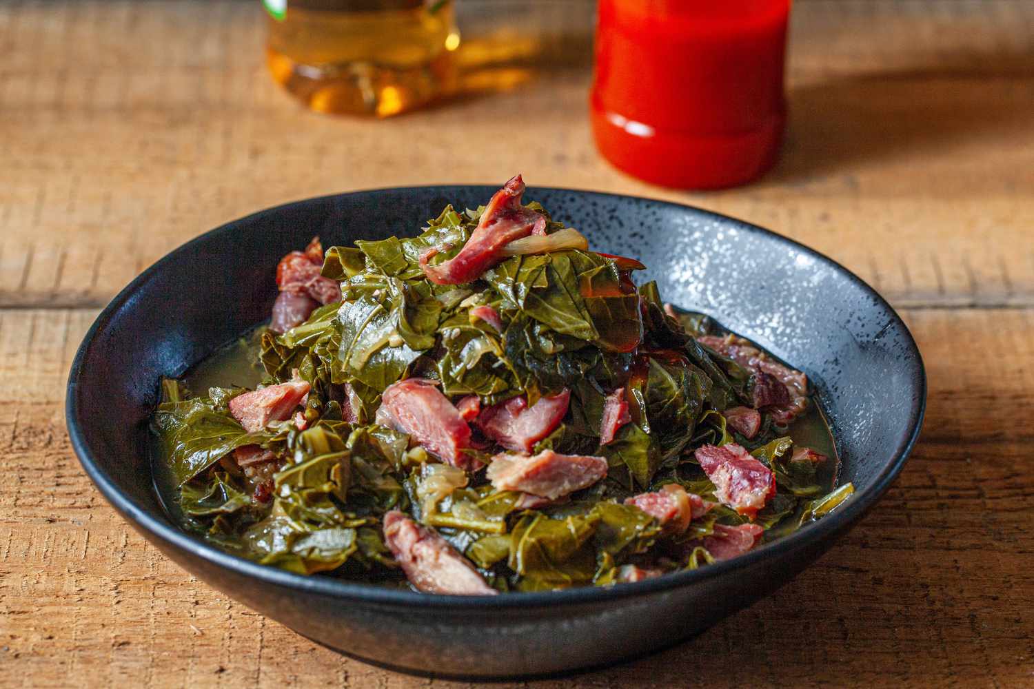 Side view of a bowl of southern collard greens in a black bowl on a wood surface.