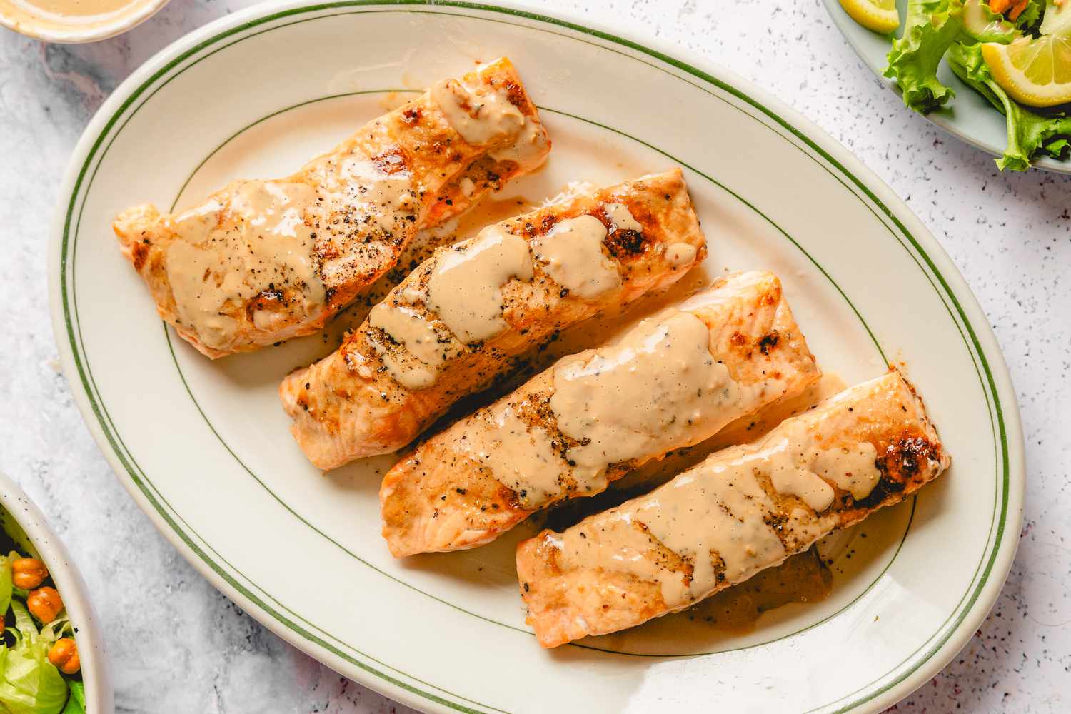 Four salmon fillets garnished with sauce on an oval plate
