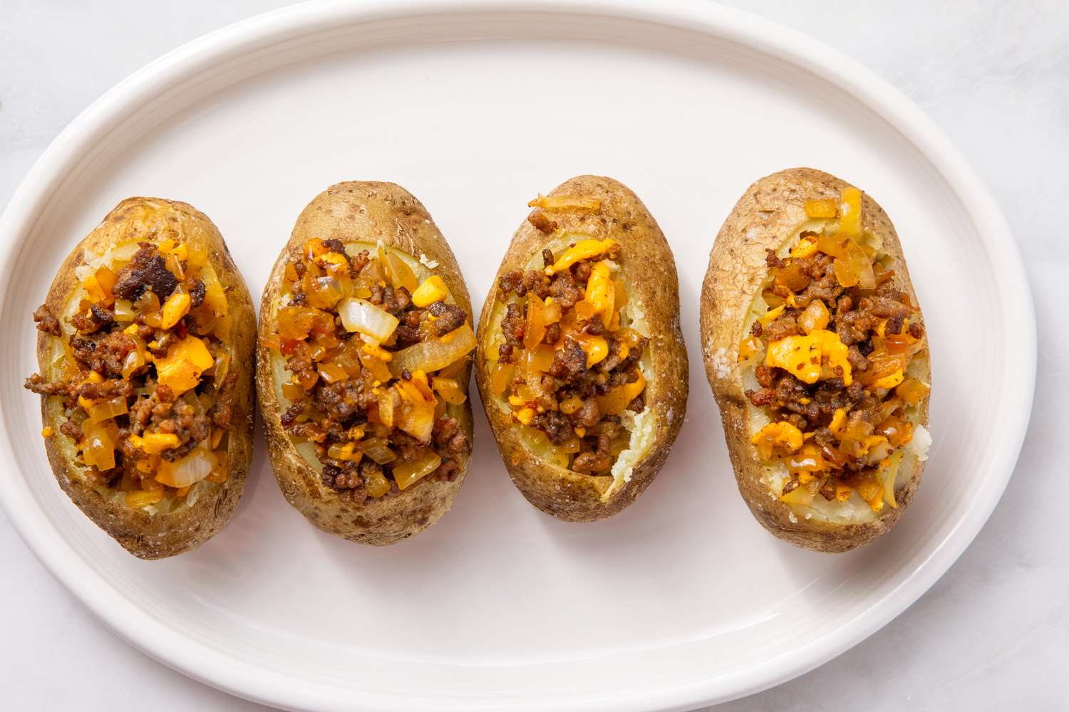 Four halved potatoes loaded with a filling of ground meat onions and cheese arranged neatly on a white plate