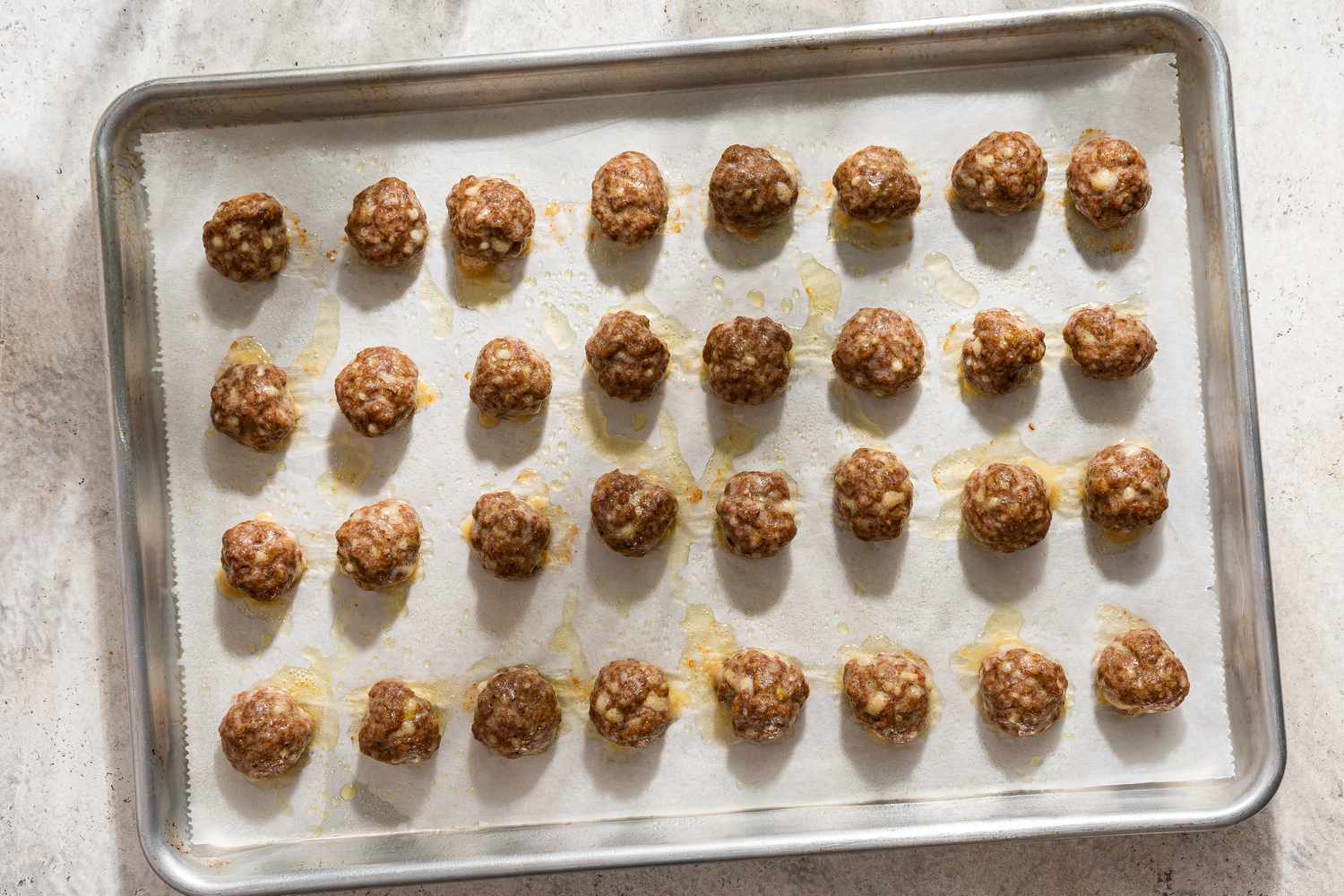 Overhead view of a large cookie sheet with cooked meatballs arranged in a grid on parchment paper for for Italian Meatball Soup recipe