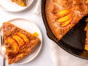 Slices of peach skillet cake on plates and in a cast iron pan served on a light background