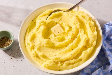 Mashed potatoes in a bowl topped with a piece of butter and black pepper a spoon placed in the dish