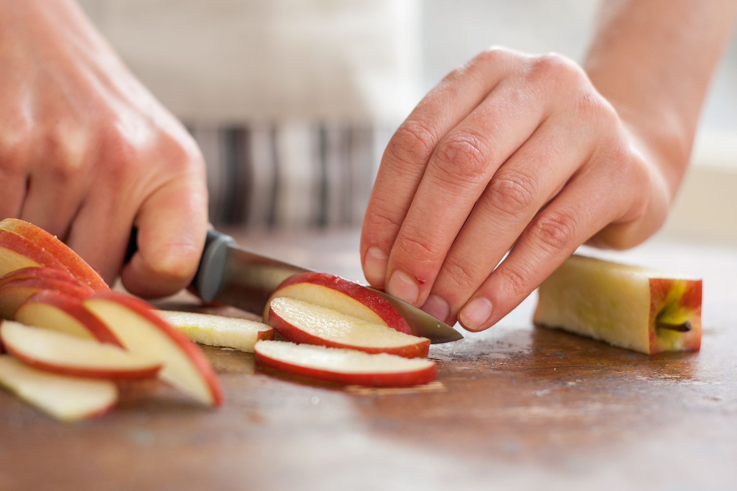 A person slicing apples on a wooden surface