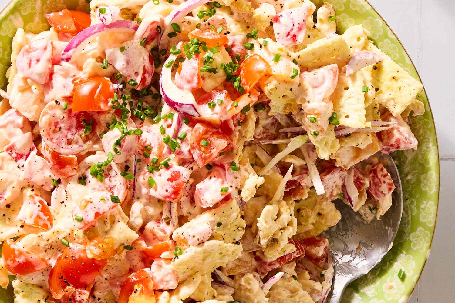 A tomato cracker salad garnished with chives, served in a bowl with a spoon