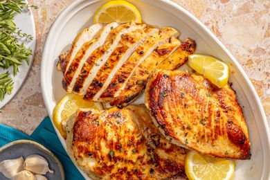 Marinated chicken breasts on a white platter with lemon slices