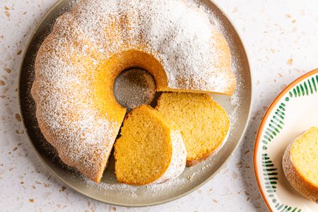 ciambellone on a platter with some of it cut into slices, and next to the platter, a slice on a plate 