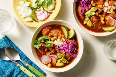 Pozole rojo served in two bowls with garnishes on a plate and a blue napkin nearby