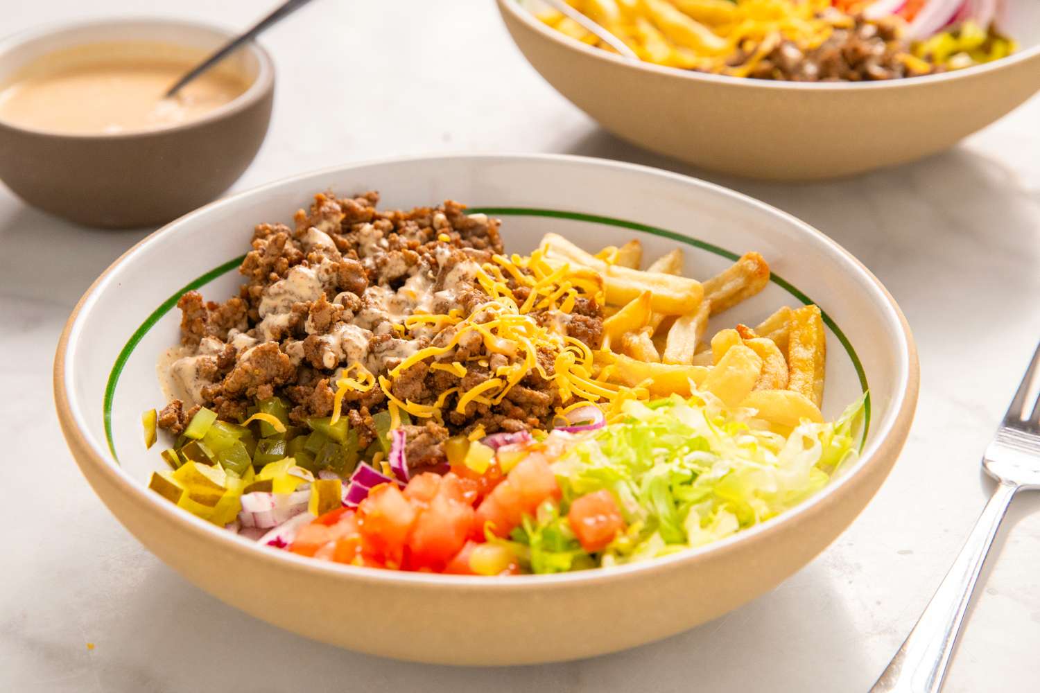 A bowl of a burgerinspired salad with ground beef shredded cheese lettuce chopped vegetables and sauce served with fries