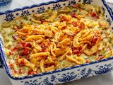 Green bean casserole in a decorative baking dish topped with crispy fried onions and red peppers