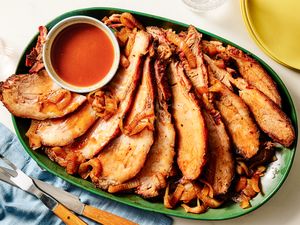 A platter of sliced brisket with onions and a dipping sauce in a small bowl