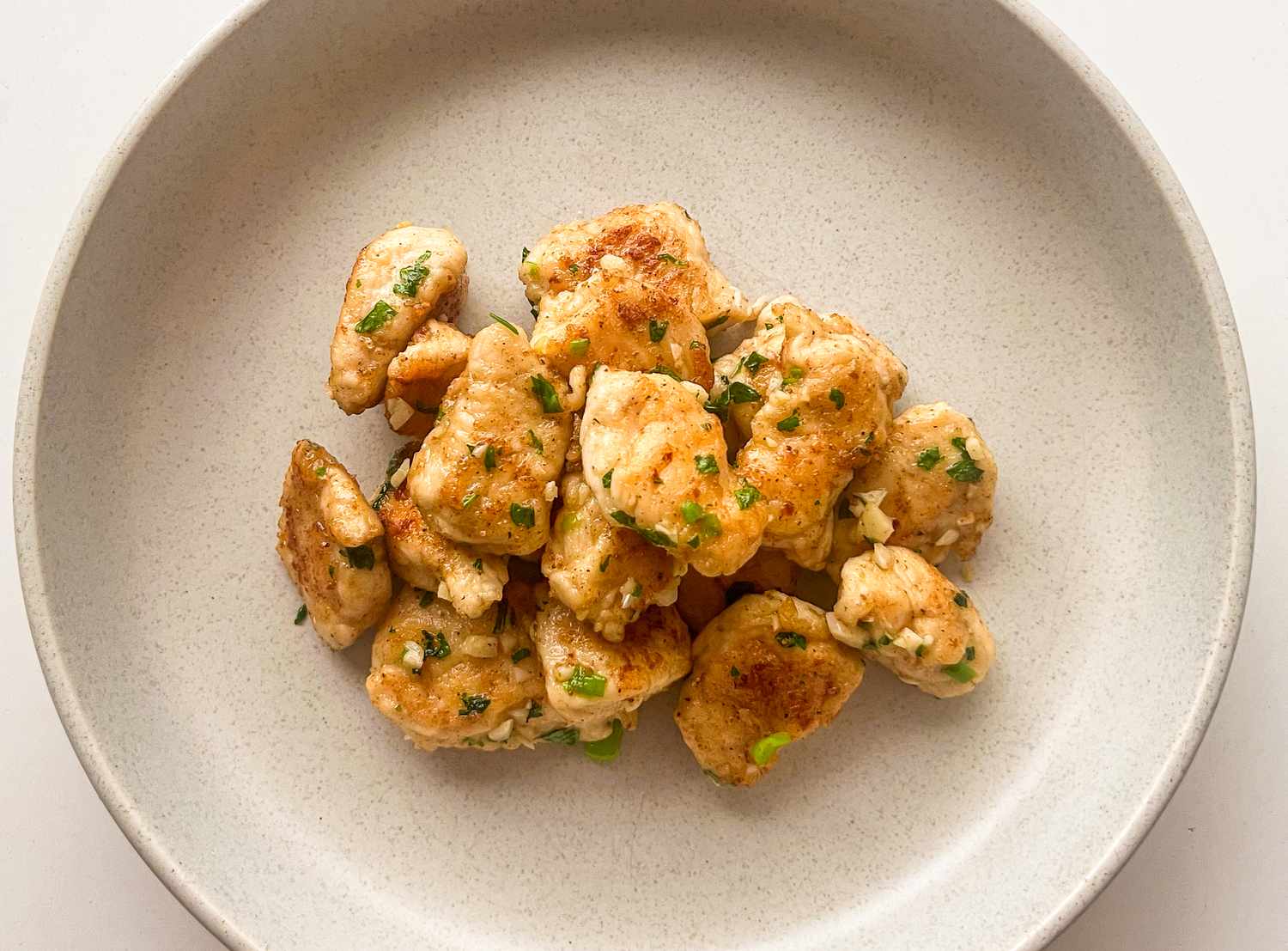 A plate of cooked chicken pieces garnished with herbs served on a white dish