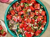 A watermelon and feta salad garnished with herbs in a blue bowl with a serving spoon