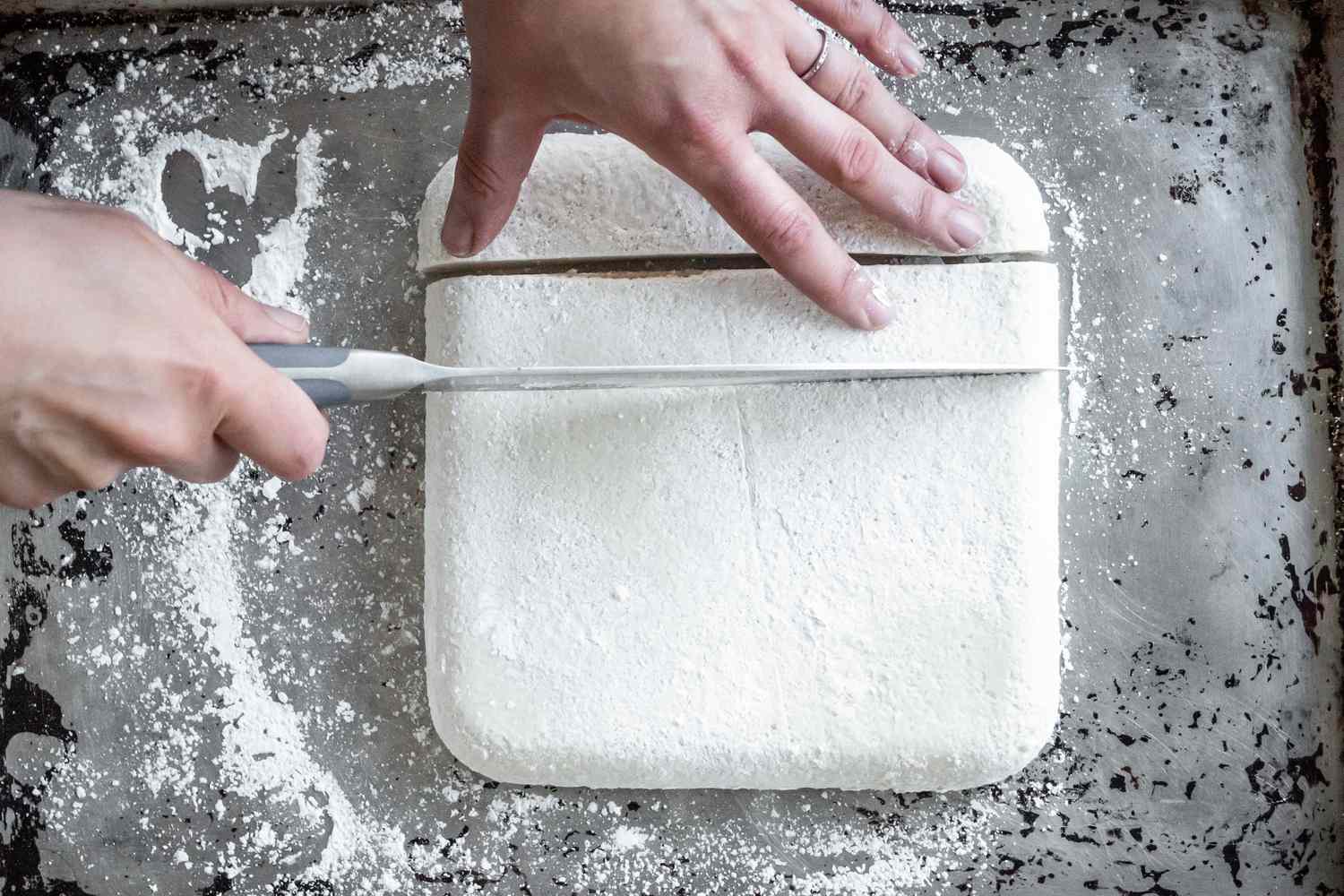 Vegan Marshmallow Block on a Baking Sheet Being Cut into Pieces Using a Knife