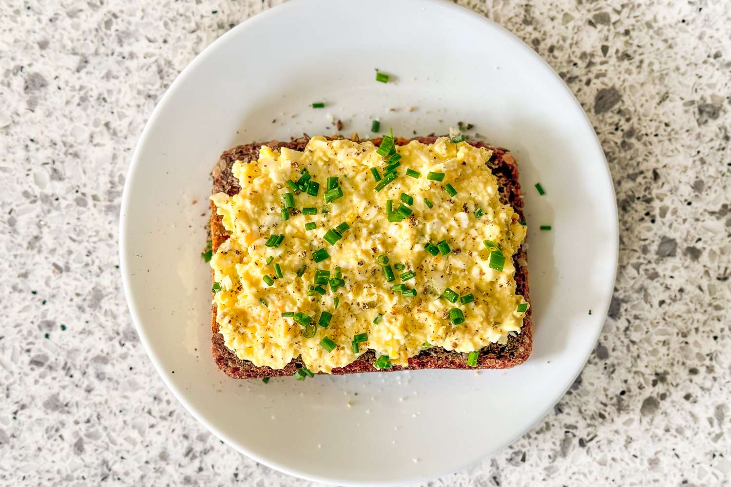 Overhead shot of a toast slice topped with egg salad on a white plate