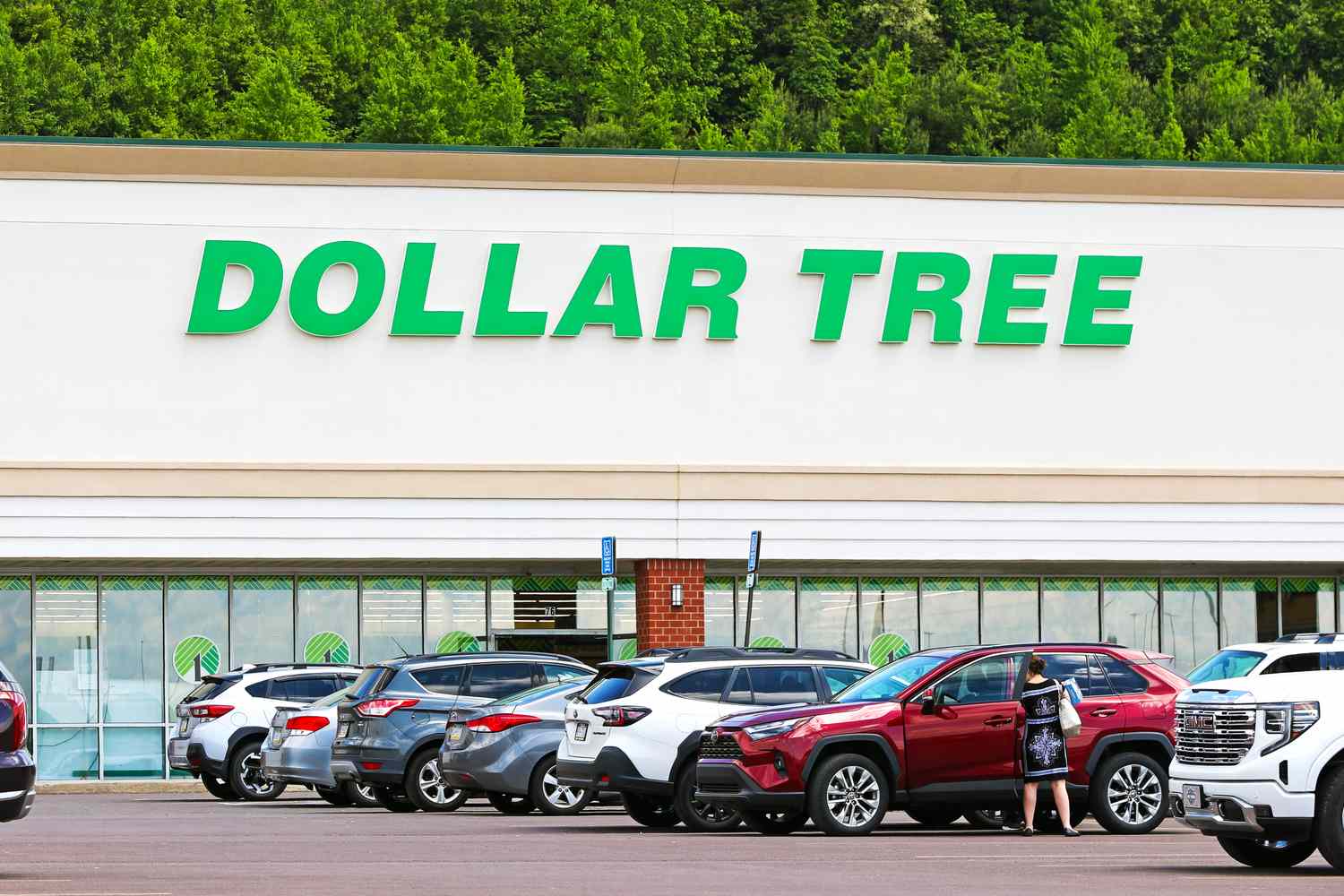 A parking lot in front of a Dollar Tree store with vehicles parked and a person standing by a car