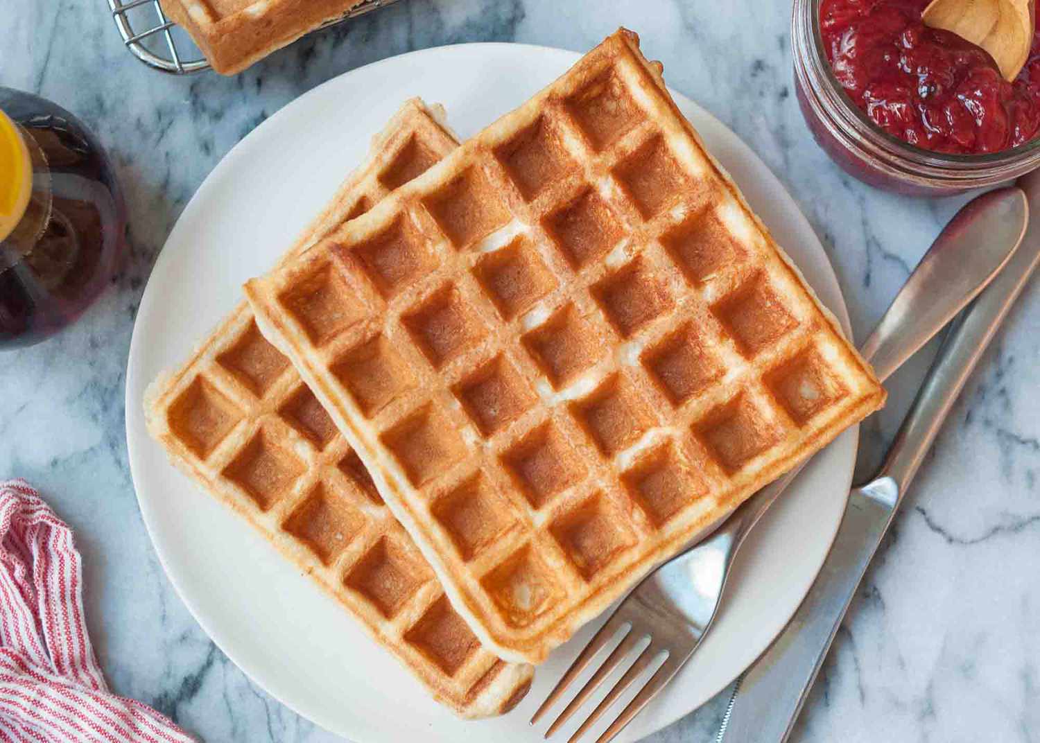 Easy waffle recipe , served on a small plate with a fork and knife nearby