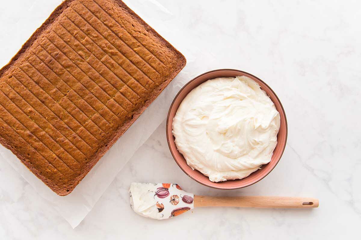 Easy Pumpkin Cake with Cream Cheese Frosting baked and set next to a bowl of cream cheese frosting.
