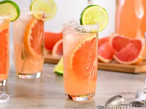 Paloma cocktail in a highbakk glass with a lime wheel garnish and cocktail ingredients in the background