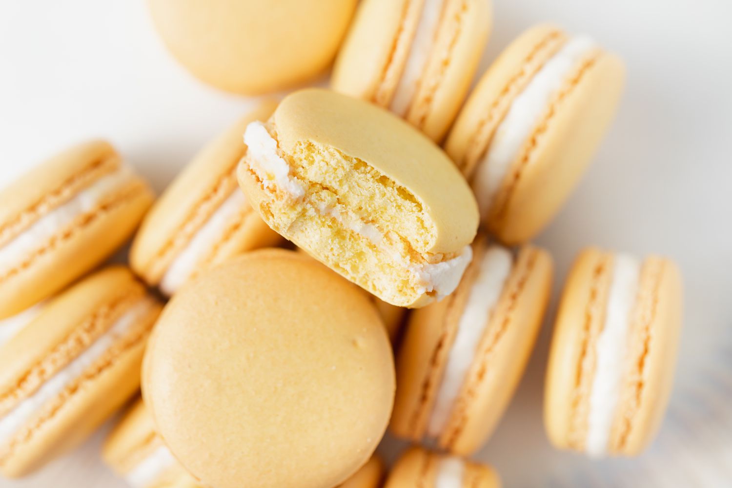 Zesty lemon buttercream macarons on a white background with the one on top that has a bite out of it.