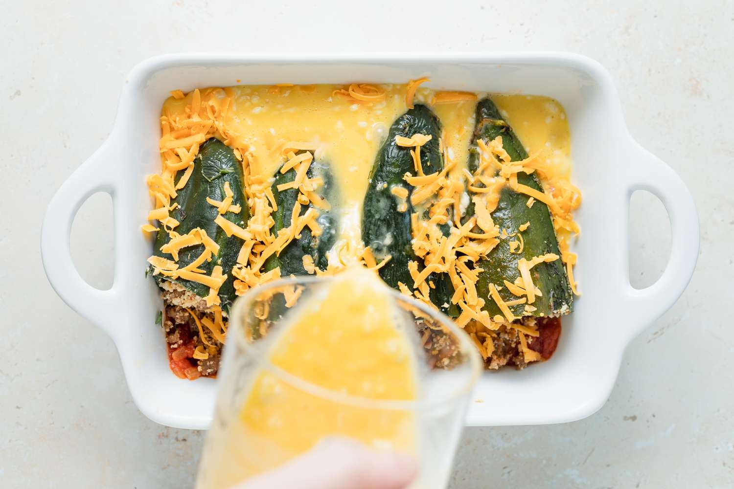 Adding cheese to top a chili relleno casserole.