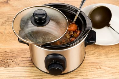 Slow cooker with stew ladle and plate on wooden table