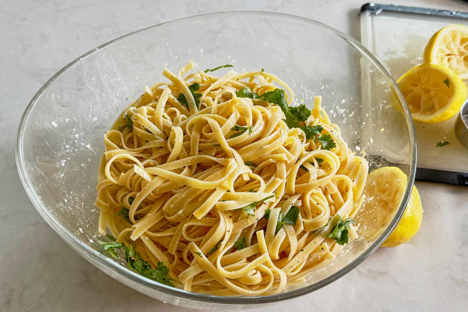 A bowl of lemon spaghetti garnished with herbs with sliced lemons on the side