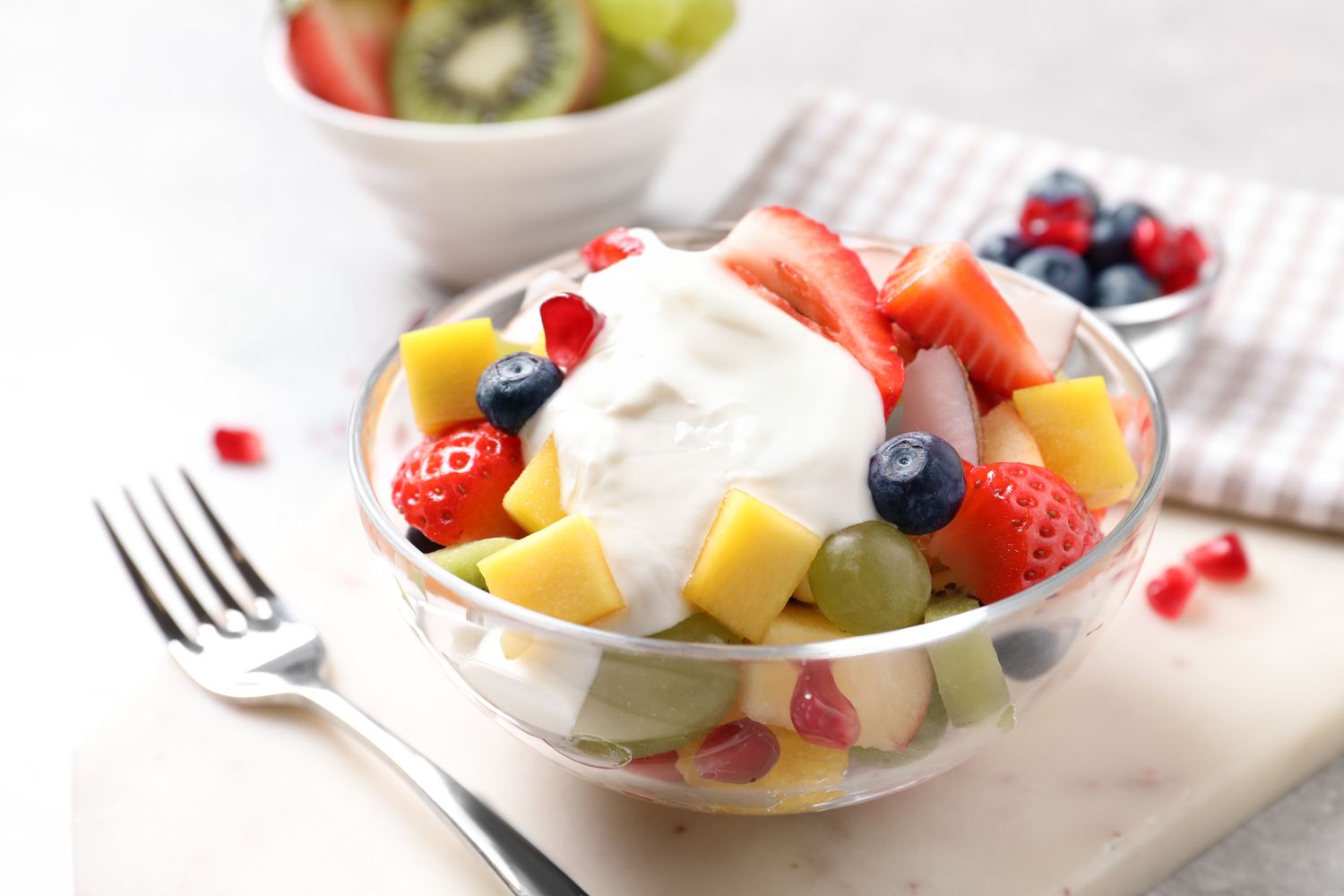 A glass bowl with fresh fruit topped with whipped cream, including strawberries, blueberries, and mango