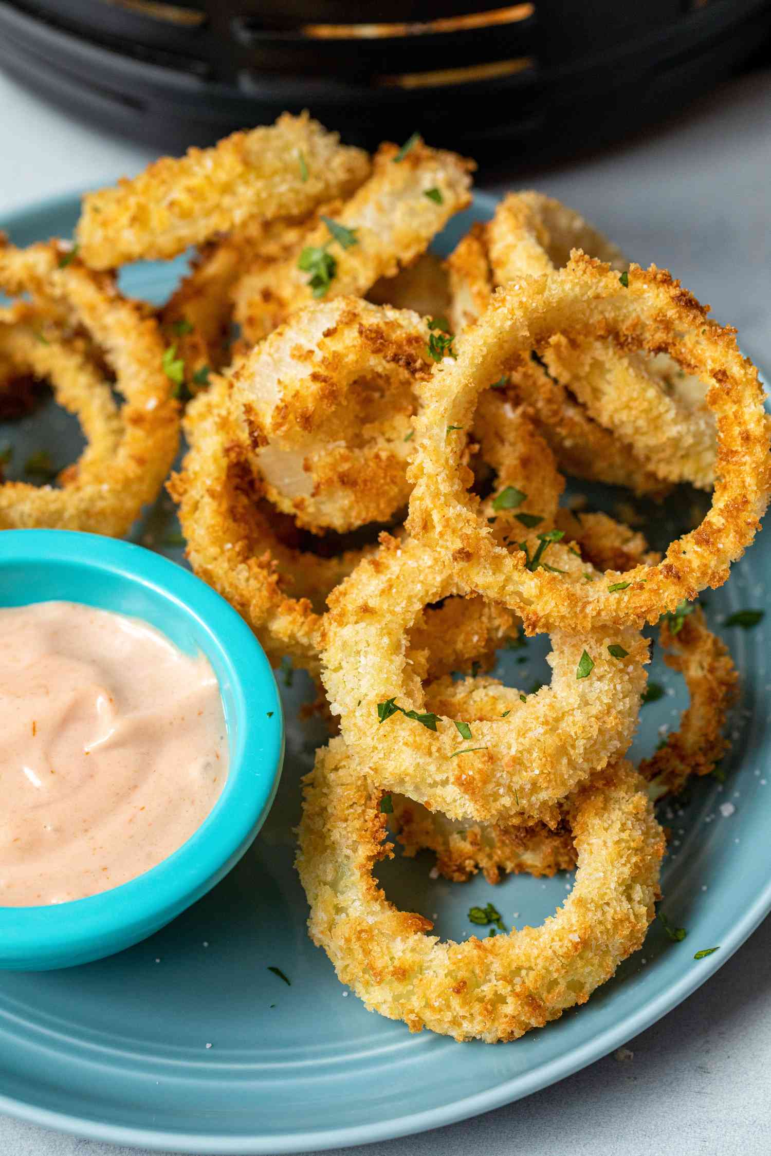 Crispy Air Fryer Onion Rings stacked on a plate with a dipping sauce.